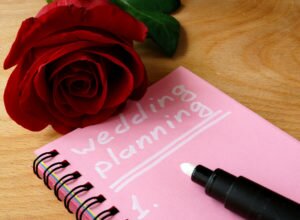 Pink notepad with wedding planning and rose on a wooden background.